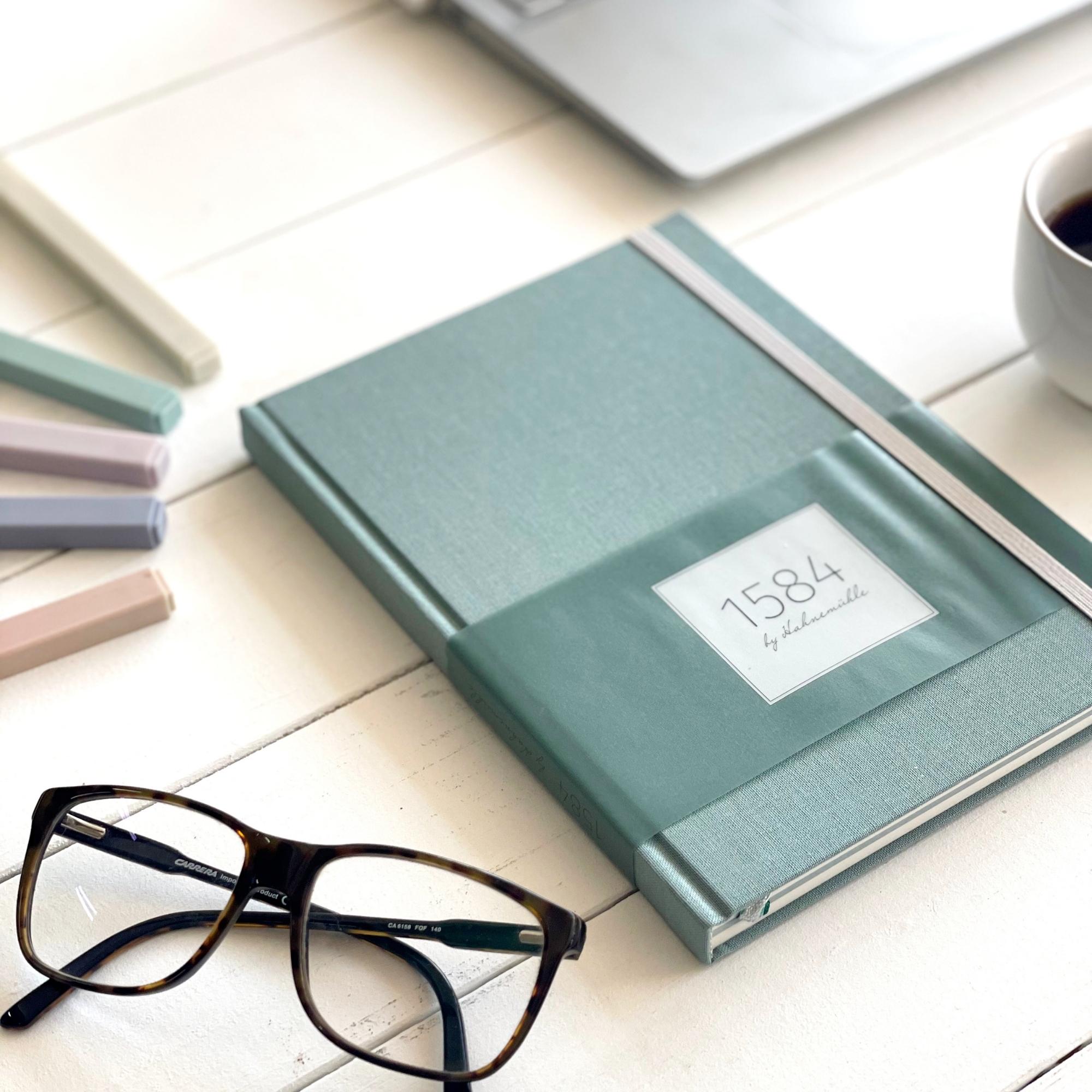 The 1584 notebook by Hahnemühle lies next to glasses on the table